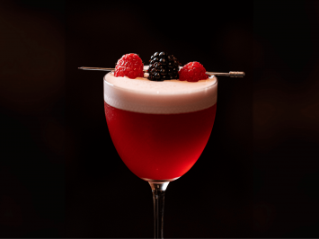 A Rouge berry cocktail served in a glass with 3 berries as a garnish