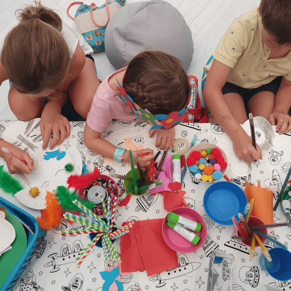 A group of children sat at a table with art supplies, drawing & creating artwork