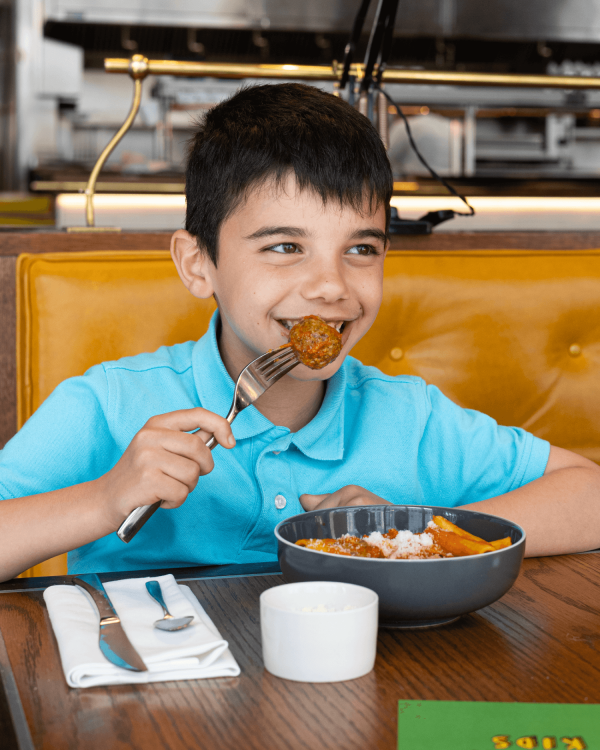 A young boy in a blue polo shirt enjoying a plate of meatballs & pasta at Bread Street Kitchen
